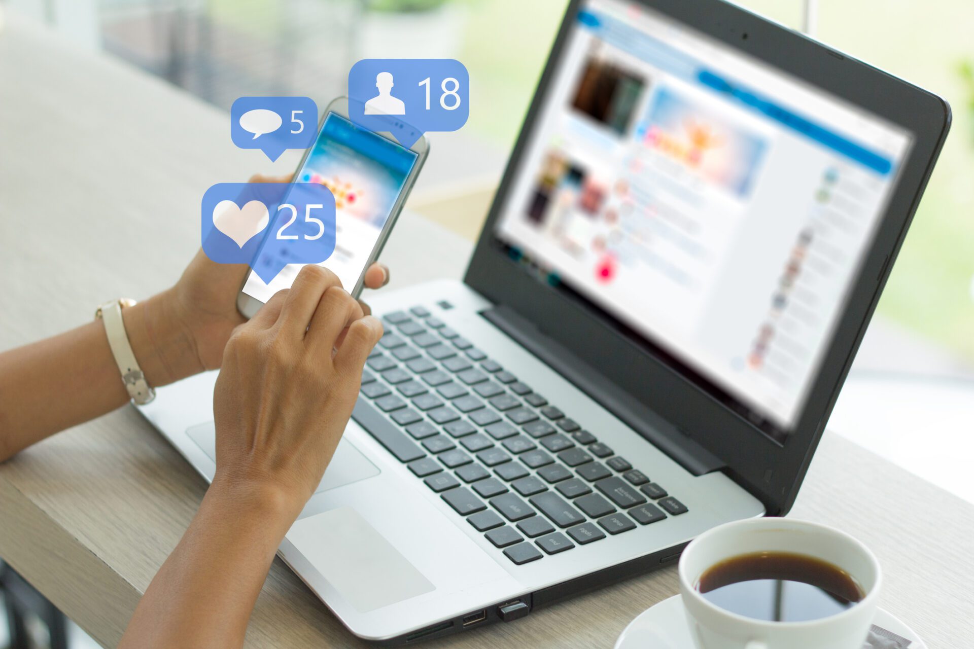 Person using smartphone with social media notifications near open laptop and cup