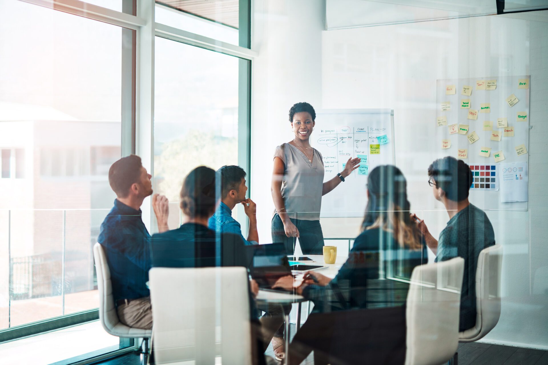 Confident businesswoman leading a presentation in a modern glass-walled conference room with a diverse team listening attentively